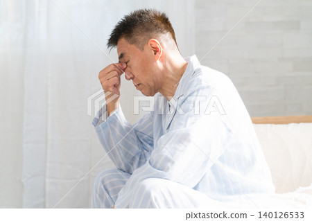 A man waking up in bed holding his eyes A man waking up in bed holding his eyes 140126533