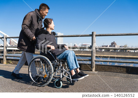 A middle-aged couple walking around pushing a wheelchair 140126552