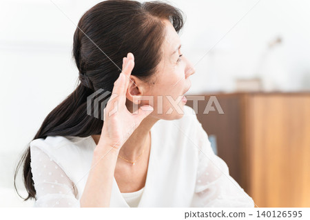 一位中年婦女用手摀住耳朵,聽著 一位中年婦女用手摀住耳朵,聽著 140126595