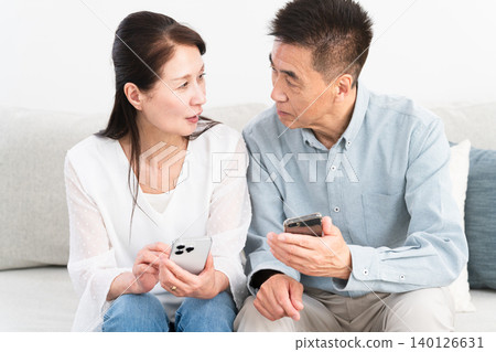 A middle-aged couple sitting on the sofa and using a smartphone Lifestyle image A middle-aged couple sitting on the sofa and using a smartphone Lifestyle image 140126631