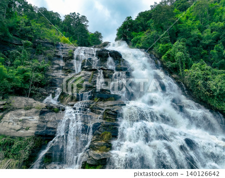 Aerial view of a waterfall in a lush tropical green forest in Doi Inthanon National Park, Chiang Mai, Thailand. This nature landscape showcases water sustainability and scenic travel destinations. Aerial view of a waterfall in a lush tropical green forest in Doi Inthanon National Park, Chiang Mai, Thailand. This nature landscape showcases water sustainability and scenic travel destinations. 140126642