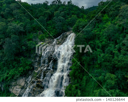 Aerial view of a waterfall in a lush tropical green forest in Doi Inthanon National Park, Chiang Mai, Thailand. This nature landscape showcases water sustainability and scenic travel destinations. Aerial view of a waterfall in a lush tropical green forest in Doi Inthanon National Park, Chiang Mai, Thailand. This nature landscape showcases water sustainability and scenic travel destinations. 140126644