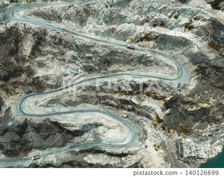 Drone shot capturing heavy machinery moving through terraced quarry levels in a limestone mine, revealing raw material extraction, land use change, and sustainability challenges in modern industry. Drone shot capturing heavy machinery moving through terraced quarry levels in a limestone mine, revealing raw material extraction, land use change, and sustainability challenges in modern industry. 140126699