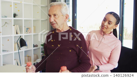 Coach guiding senior man doing arm exercises at home burgundy sweater pink top peach dumbbells Coach guiding senior man doing arm exercises at home burgundy sweater pink top peach dumbbells 140126924