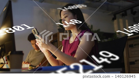 Holding woman wearing magenta tank top checking phone at office desk, with floating numbers Holding woman wearing magenta tank top checking phone at office desk, with floating numbers 140126945