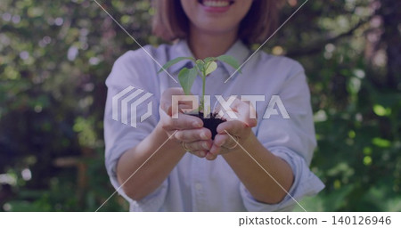 Holding Chinese woman offering seedling in garden, cupped hands holding soil, pale shirt and rings Holding Chinese woman offering seedling in garden, cupped hands holding soil, pale shirt and rings 140126946