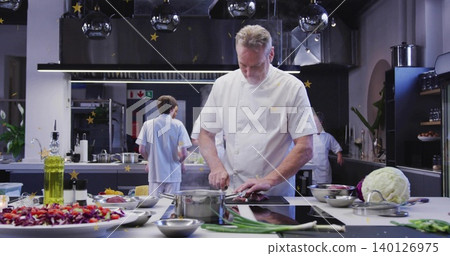 Chopping head chef wearing white jacket working at stainless prep island with cutting board, salad Chopping head chef wearing white jacket working at stainless prep island with cutting board, salad 140126975