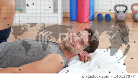 Reclining man in grey tank smiling at camera on towel in studio, with kettlebells, dotted overlay Reclining man in grey tank smiling at camera on towel in studio, with kettlebells, dotted overlay 140127077