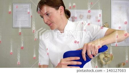 Medic in white tunic holding blue ortho cushion in clinic with spine, certificates, binary overlay 140127083