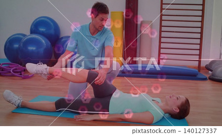 Physical therapist is stretching client leg on mat in flat design gym, with fitness icons overlay Physical therapist is stretching client leg on mat in flat design gym, with fitness icons overlay 140127337