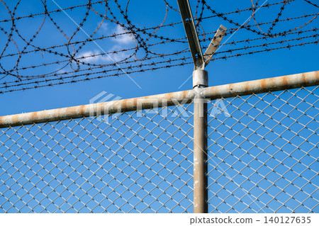 Barbed wire fence symbolizing border control, geopolitical tensions, and restricted freedoms in modern society. Barbed wire border security fence. Barrier border. Boundary security wall. Private area. Barbed wire fence symbolizing border control, geopolitical tensions, and restricted freedoms in modern society. Barbed wire border security fence. Barrier border. Boundary security wall. Private area. 140127635
