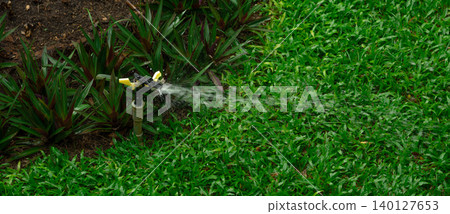 Automatic lawn sprinkler system watering green grass in residential garden with water droplets splashing. Landscape maintenance and conservation. Automatic watering system technology. Water saving. Automatic lawn sprinkler system watering green grass in residential garden with water droplets splashing. Landscape maintenance and conservation. Automatic watering system technology. Water saving. 140127653