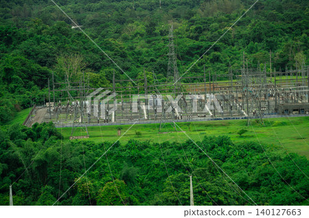 Electrical power station at hydroelectric dam facility with green forest. Sustainable renewable energy infrastructure technology. Power transmission substation near dam. Sustainable power generation. 140127663