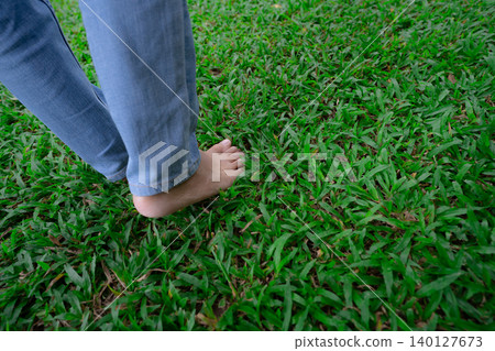 Close-up of barefoot person stepping on lush green grass lawn. Nature connection and natural healing through walking outdoors. Peaceful wellness retreat. Mindful lifestyle and connection to the earth. Close-up of barefoot person stepping on lush green grass lawn. Nature connection and natural healing through walking outdoors. Peaceful wellness retreat. Mindful lifestyle and connection to the earth. 140127673