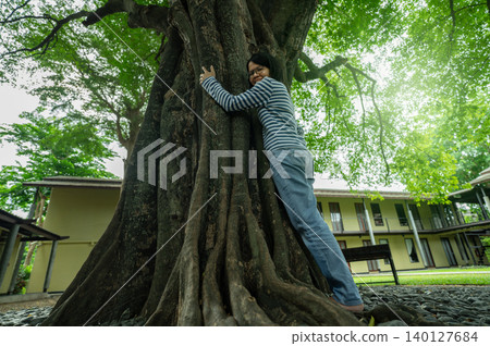 Asian woman hugging big tree trunk. Eco retreat. Nature connection therapy for mental health wellness and digital detox healing in natural environment. Mental wellness and digital detox at eco hotel. Asian woman hugging big tree trunk. Eco retreat. Nature connection therapy for mental health wellness and digital detox healing in natural environment. Mental wellness and digital detox at eco hotel. 140127684