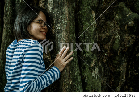 Woman practicing forest therapy mindfulness meditation leaning face against tree trunk. Digital detox retreat. Spiritual healing and natural wellness. Reconnecting with nature. Forest bathing therapy. 140127685