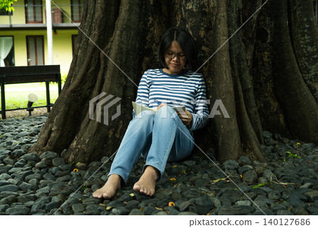 Woman writing in notebook under the old tree. Self-reflection, goal setting, journaling habit, and mindful planning. Creativity, life planning, and focus on personal growth. Mindful practice. Woman writing in notebook under the old tree. Self-reflection, goal setting, journaling habit, and mindful planning. Creativity, life planning, and focus on personal growth. Mindful practice. 140127686