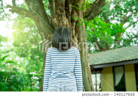 Rear view of woman looking up at a big tree in hotel garden. Sustainable retreat. Eco travel. Mindfulness, nature connection, and sustainable tourism during a wellness-inspired vacation retreat. Rear view of woman looking up at a big tree in hotel garden. Sustainable retreat. Eco travel. Mindfulness, nature connection, and sustainable tourism during a wellness-inspired vacation retreat. 140127688