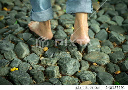 Close-up of barefoot woman walking on gravel ground in a peaceful forest retreat during early morning light. Self-care, emotional healing, and connection with nature for mental balance. Mindfulness. Close-up of barefoot woman walking on gravel ground in a peaceful forest retreat during early morning light. Self-care, emotional healing, and connection with nature for mental balance. Mindfulness. 140127691