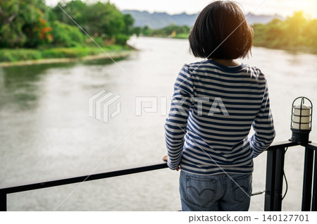 Rear view of a woman gazing at calm river. Travel retreat. Peaceful solitude, personal reflection. Nature connection. Freedom, and emotional healing. Rest, and inner clarity. Emotional balance. Rear view of a woman gazing at calm river. Travel retreat. Peaceful solitude, personal reflection. Nature connection. Freedom, and emotional healing. Rest, and inner clarity. Emotional balance. 140127701