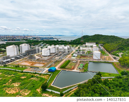 Gas storage tanks in lush green hill and forest. Industrial petrochemical facility with extensive steel pipeline network and water reservoir. Energy infrastructure balancing with natural environment. Gas storage tanks in lush green hill and forest. Industrial petrochemical facility with extensive steel pipeline network and water reservoir. Energy infrastructure balancing with natural environment. 140127831