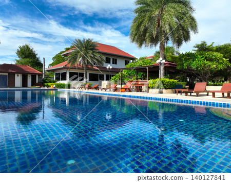 Serene luxury hotel infinity pool nestled within tropical vegetation with placed comfortable loungers offering guests private relaxation spots during daytime at exclusive island getaway destination. Serene luxury hotel infinity pool nestled within tropical vegetation with placed comfortable loungers offering guests private relaxation spots during daytime at exclusive island getaway destination. 140127841