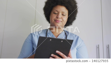 Holding black clipboard, nurse reviewing notes at clinic, wearing light blue scrubs and stethoscope Holding black clipboard, nurse reviewing notes at clinic, wearing light blue scrubs and stethoscope 140127935