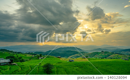 Sunset casts golden light over rolling green hills and rice terrace fields with rural village in the mountains. Eco living and sustainable agriculture. Organic farming. Beauty of sustainable living. Sunset casts golden light over rolling green hills and rice terrace fields with rural village in the mountains. Eco living and sustainable agriculture. Organic farming. Beauty of sustainable living. 140128094