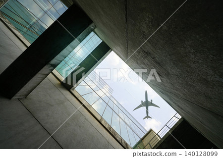Commercial airplane flying above sustainable glass skyscraper. Cargo aircraft flying over contemporary eco friendly glass office building. Global transportation logistics and sustainable architecture. Commercial airplane flying above sustainable glass skyscraper. Cargo aircraft flying over contemporary eco friendly glass office building. Global transportation logistics and sustainable architecture. 140128099