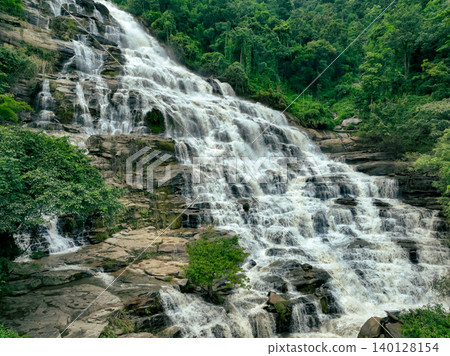 Aerial view of a waterfall in a lush tropical green forest in Doi Inthanon National Park, Chiang Mai, Thailand. This nature landscape showcases water sustainability and scenic travel destinations. Aerial view of a waterfall in a lush tropical green forest in Doi Inthanon National Park, Chiang Mai, Thailand. This nature landscape showcases water sustainability and scenic travel destinations. 140128154