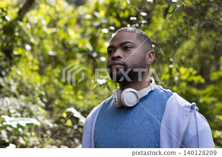 African American man wearing hoodie and headphones standing amid lush forest, copy space African American man wearing hoodie and headphones standing amid lush forest, copy space 140128209