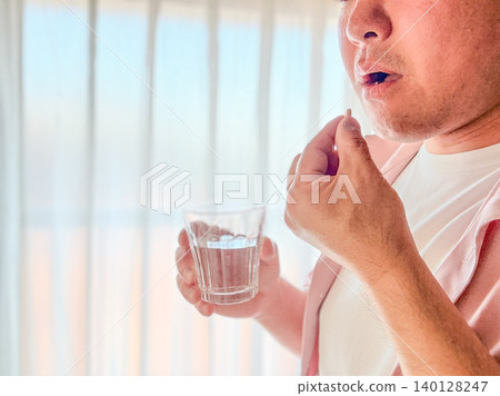 A middle-aged man takes his medicine with water. 140128247