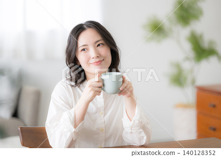 A smiling woman with a mug in her relaxed morning lifestyle, upper body facing the camera. A smiling woman with a mug in her relaxed morning lifestyle, upper body facing the camera. 140128352