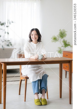 一位微笑的女士手捧馬克杯,展現出輕鬆的晨間生活狀態,上半身面向鏡頭。 一位微笑的女士手捧馬克杯,展現出輕鬆的晨間生活狀態,上半身面向鏡頭。 140128353