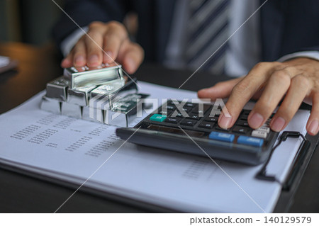 Silver Bullion Investment and Financial Analysis. Businessman Calculating Investment Returns with Silver Bars and Financial Documents. Silver Bullion Investment and Financial Analysis. Businessman Calculating Investment Returns with Silver Bars and Financial Documents. 140129579