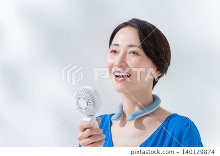 A woman using an ice ring and a handheld fan in the summer. 140129874