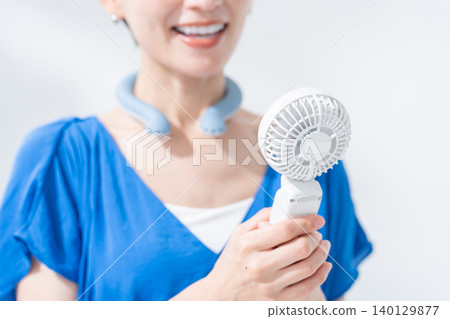 A woman using an ice ring and a handheld fan in the summer. A woman using an ice ring and a handheld fan in the summer. 140129877