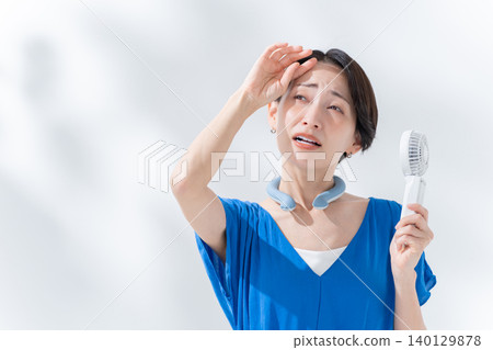 A woman using an ice ring and a handheld fan in the summer. A woman using an ice ring and a handheld fan in the summer. 140129878