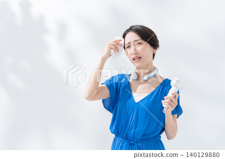 A woman using an ice ring and a handheld fan in the summer. A woman using an ice ring and a handheld fan in the summer. 140129880