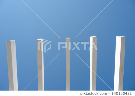 Abstract geometric pattern of white parallel sunshade poles with extensive negative space. Minimalist architectural background with white wooden beams and clear blue sky copy space. Abstract geometric pattern of white parallel sunshade poles with extensive negative space. Minimalist architectural background with white wooden beams and clear blue sky copy space. 140130481