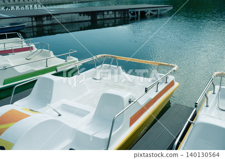 High angle view of white and yellow pedal boats parked at a modern pier on a calm lake, summer vacation and park recreation concept. High angle view of white and yellow pedal boats parked at a modern pier on a calm lake, summer vacation and park recreation concept. 140130564