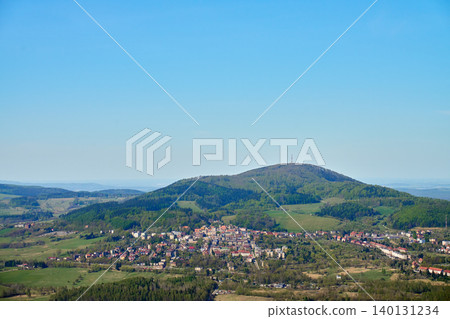 Small town sits below a green wooded hill with fields, rooftops and clear blue sky. Concept of countryside travel, rural landscape and tourism. Small town sits below a green wooded hill with fields, rooftops and clear blue sky. Concept of countryside travel, rural landscape and tourism. 140131234