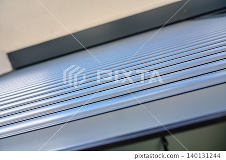 Closeup of a grey exterior roller shutter with horizontal metal slats installed above a modern house window. Closeup of a grey exterior roller shutter with horizontal metal slats installed above a modern house window. 140131244
