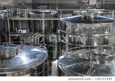 Elevated overhead view showing multiple heavy industrial stainless steel fermentation storage tanks inside spacious modern manufacturing facility processing liquid commercial products Elevated overhead view showing multiple heavy industrial stainless steel fermentation storage tanks inside spacious modern manufacturing facility processing liquid commercial products 140131495