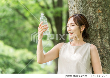 一位神態輕鬆的女士正在喝瓶裝水、礦泉水和熱水。 一位神態輕鬆的女士正在喝瓶裝水、礦泉水和熱水。 140131726