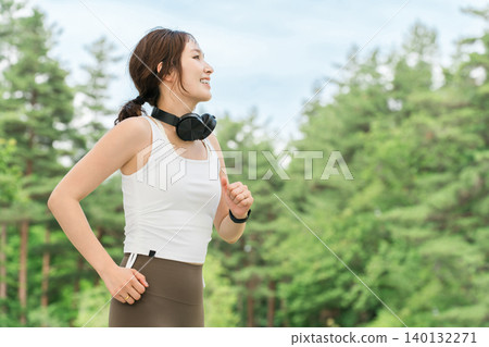 A woman wearing headphones running, walking, jogging, or exercising in a park (dieting, sports) A woman wearing headphones running, walking, jogging, or exercising in a park (dieting, sports) 140132271