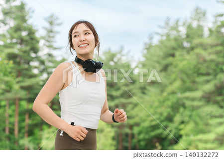 A woman wearing headphones running, walking, jogging, or exercising in a park (dieting, sports) A woman wearing headphones running, walking, jogging, or exercising in a park (dieting, sports) 140132272