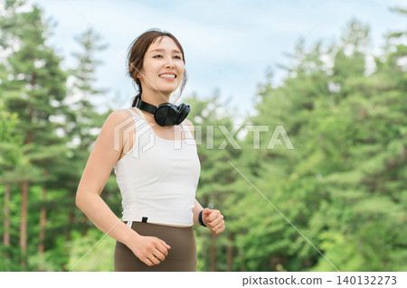 A woman wearing headphones running, walking, jogging, or exercising in a park (dieting, sports) A woman wearing headphones running, walking, jogging, or exercising in a park (dieting, sports) 140132273