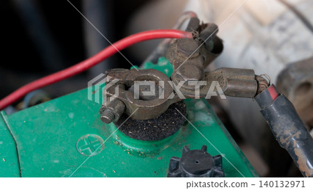 Close-up of highlights the rusted positive metal clamp attached to the green car battery terminal. The worn connection demonstrates electrical wear and tear and requires regular engine maintenance. Close-up of highlights the rusted positive metal clamp attached to the green car battery terminal. The worn connection demonstrates electrical wear and tear and requires regular engine maintenance. 140132971
