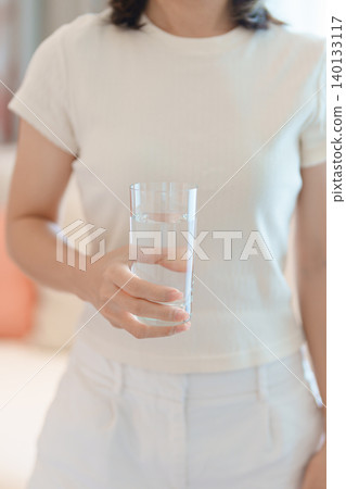 Healthy woman hold glass of clean mineral water glass on sofa at home, female drink pure water for hydration and wellness, fresh skin care, daily routine water intake, Refreshment and lifestyle Healthy woman hold glass of clean mineral water glass on sofa at home, female drink pure water for hydration and wellness, fresh skin care, daily routine water intake, Refreshment and lifestyle 140133117